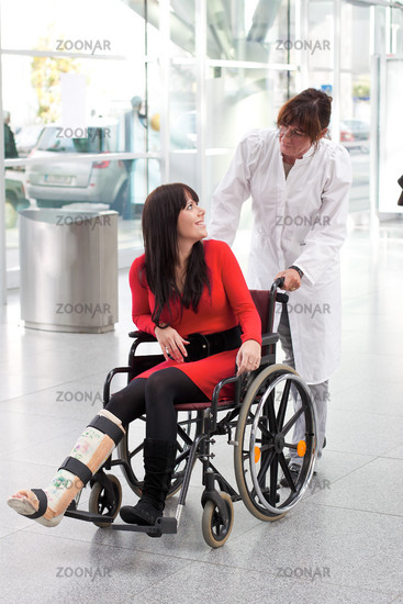 Junge Frau mit Gipsbein Rollstuhl und Pflegerin